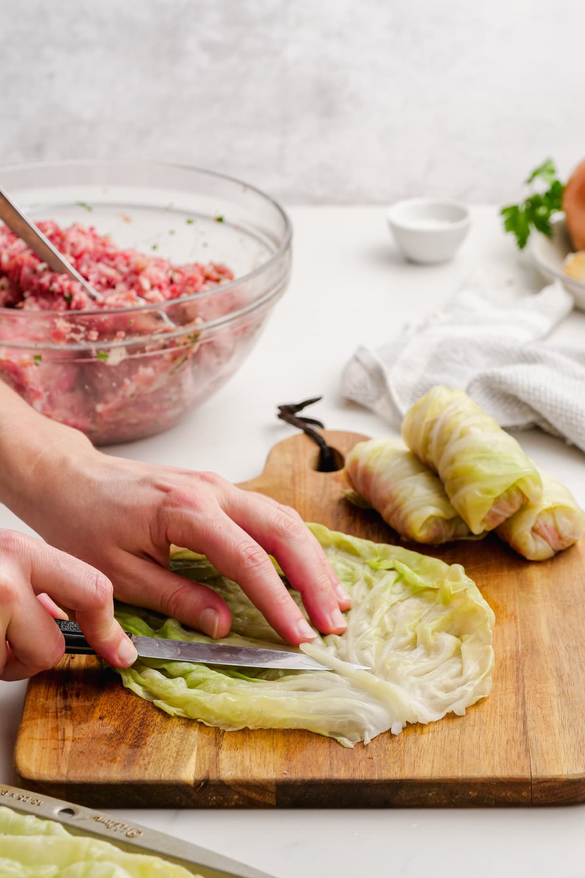 woman's hand trimming cabbage roll core from cooked leaf with a knife