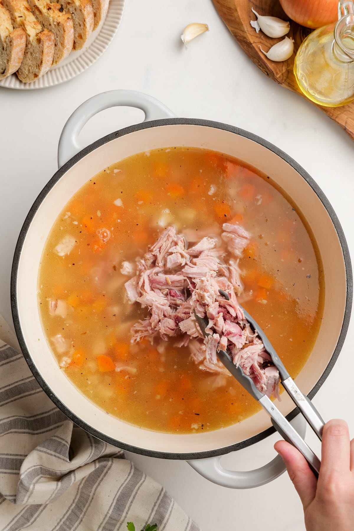 woman's hand placing shredded ham back in pot of ham and bean soup with tongs