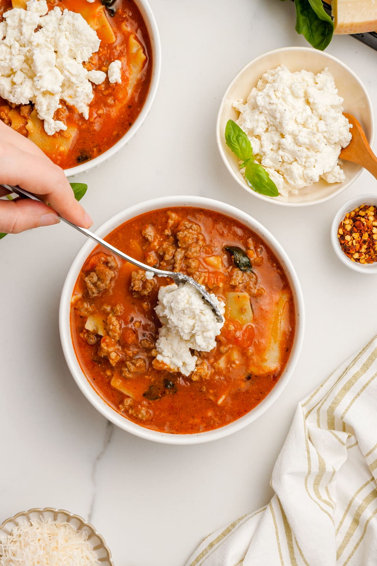 Woman's hand spooning ricotta and cheese mixture into bowl of lasagna soup