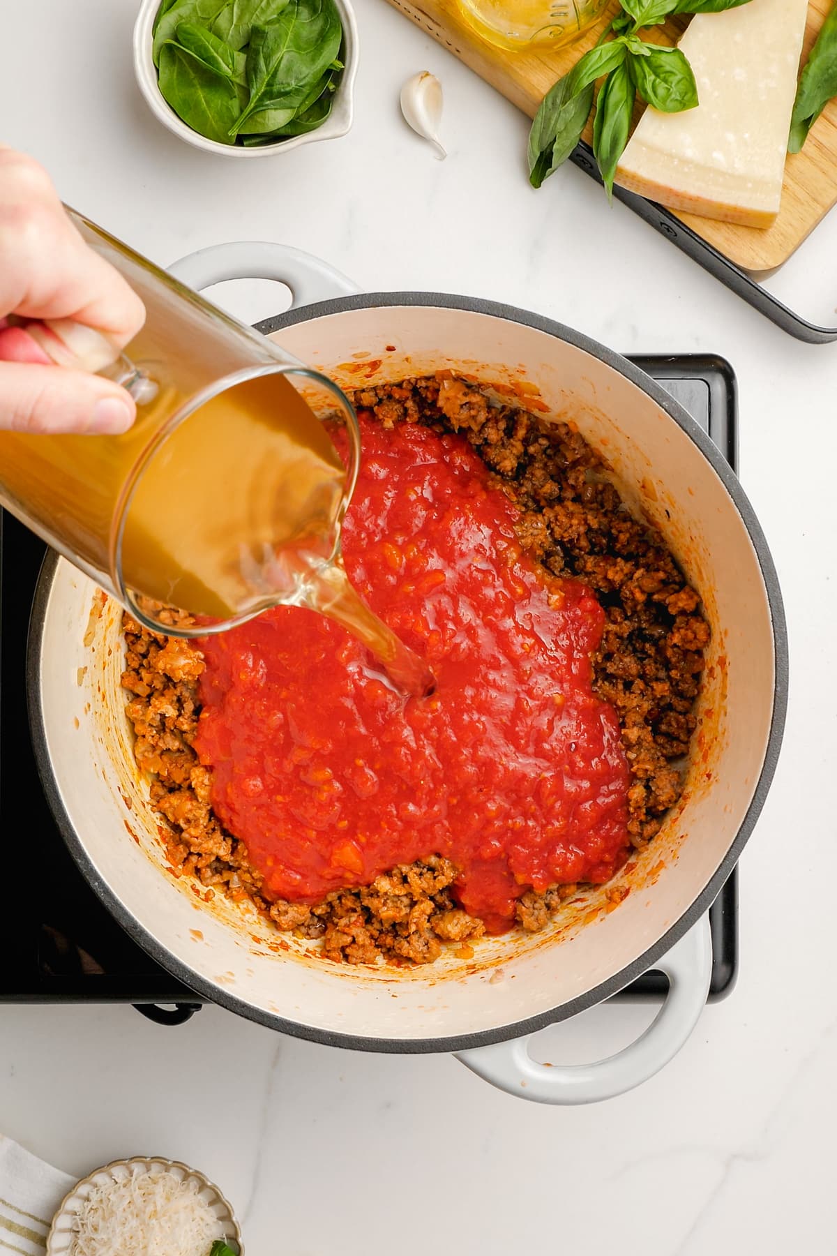Woman's hand pouring broth into a saucepan with cooked lasagna soup ingredients
