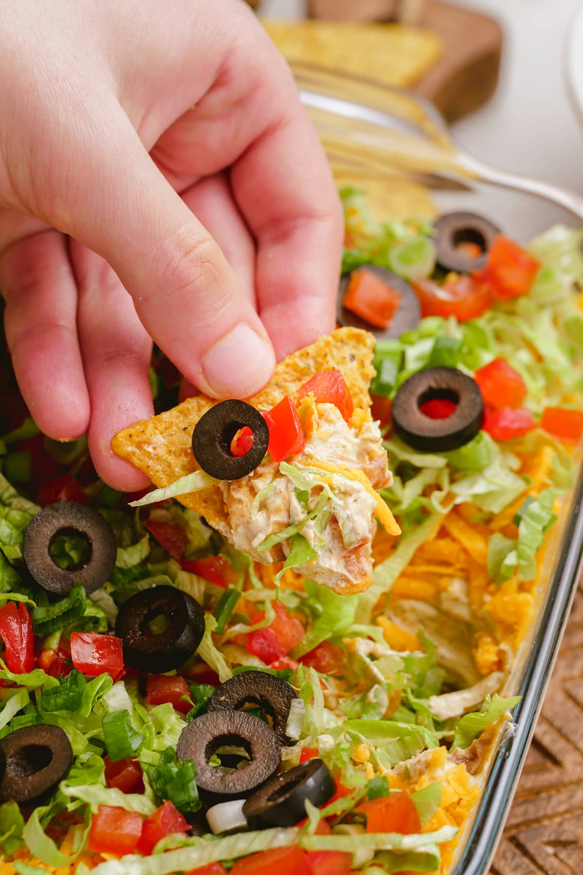 woman's hand dipping tortilla chip into taco dip in casserole dish on tablescape