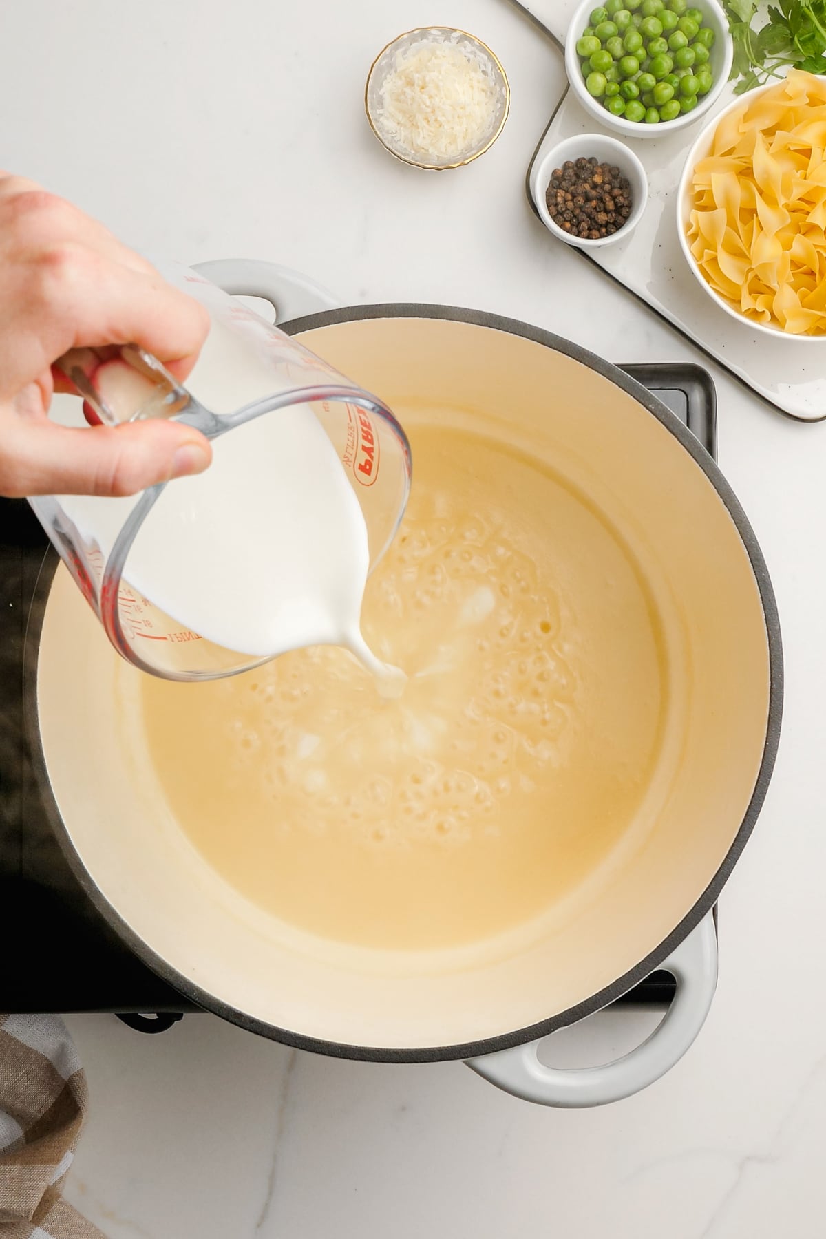 woman's hand pouring milk into pot with roux