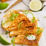 styled quesadilla triangles on a plate with shredded lettuce, dollop of sour cream and lime wedge.