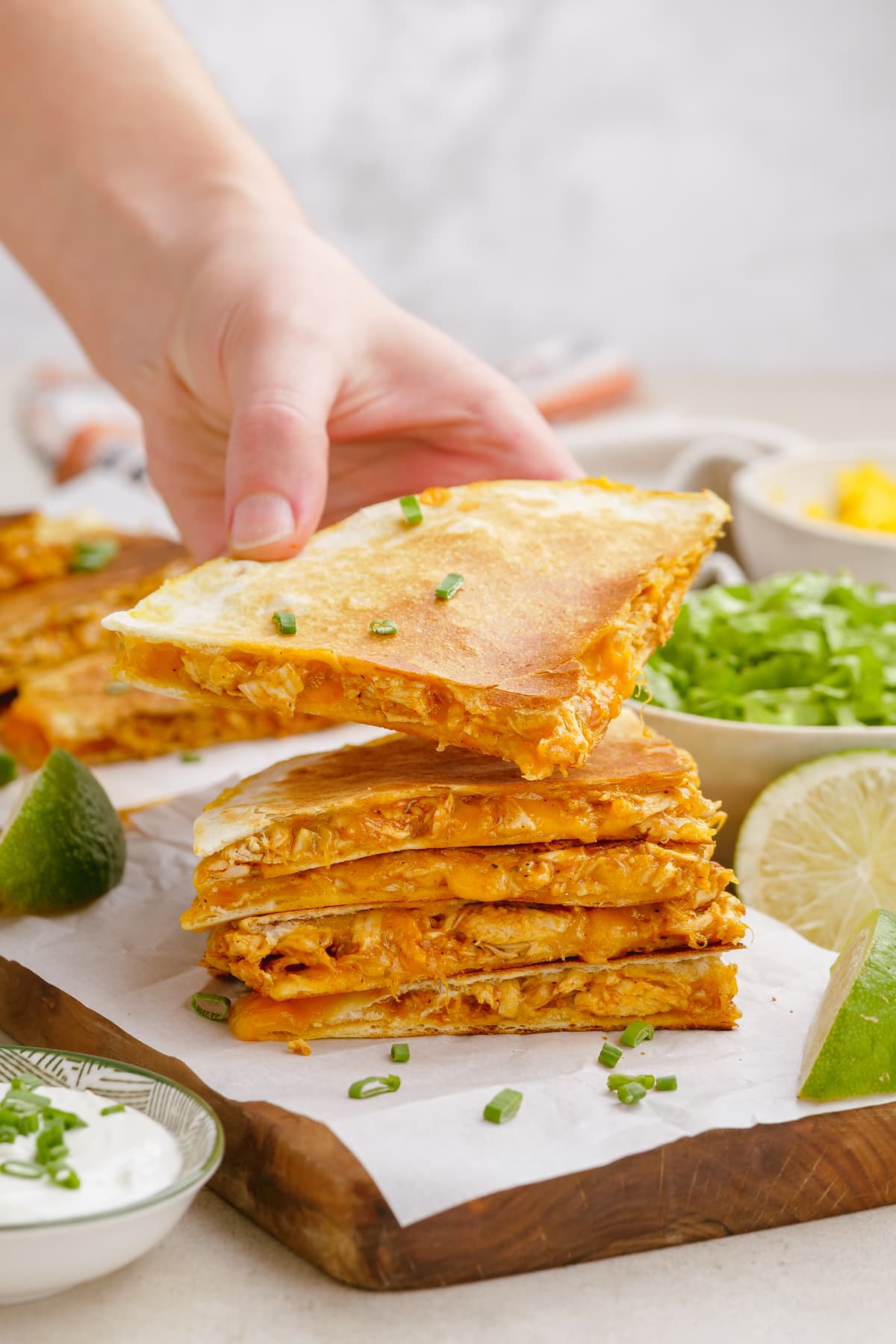 woman's hand holding a quesadilla triangle with stack of quesadilla triangle below