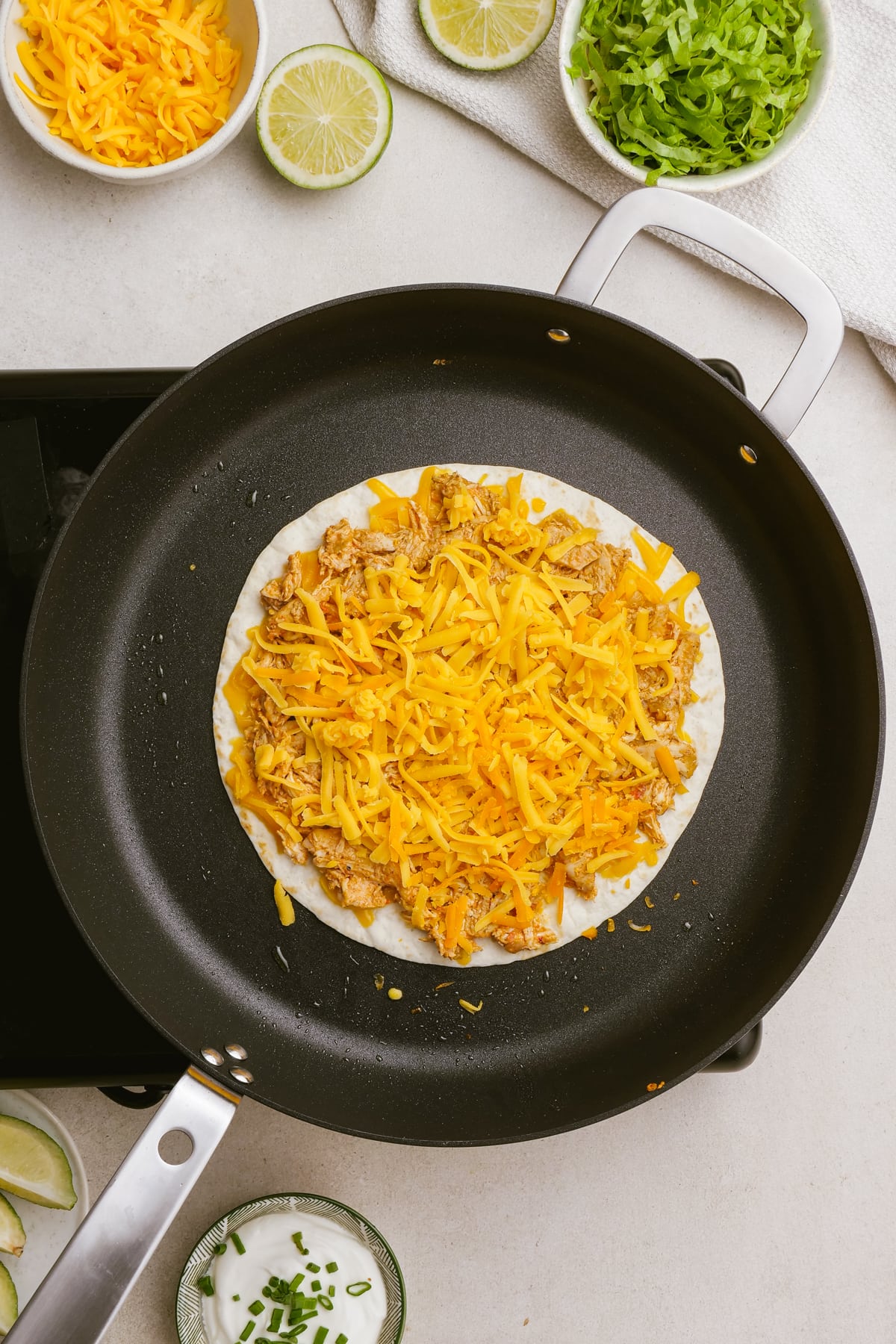 tortilla on skillet with shredded cheese and chicken