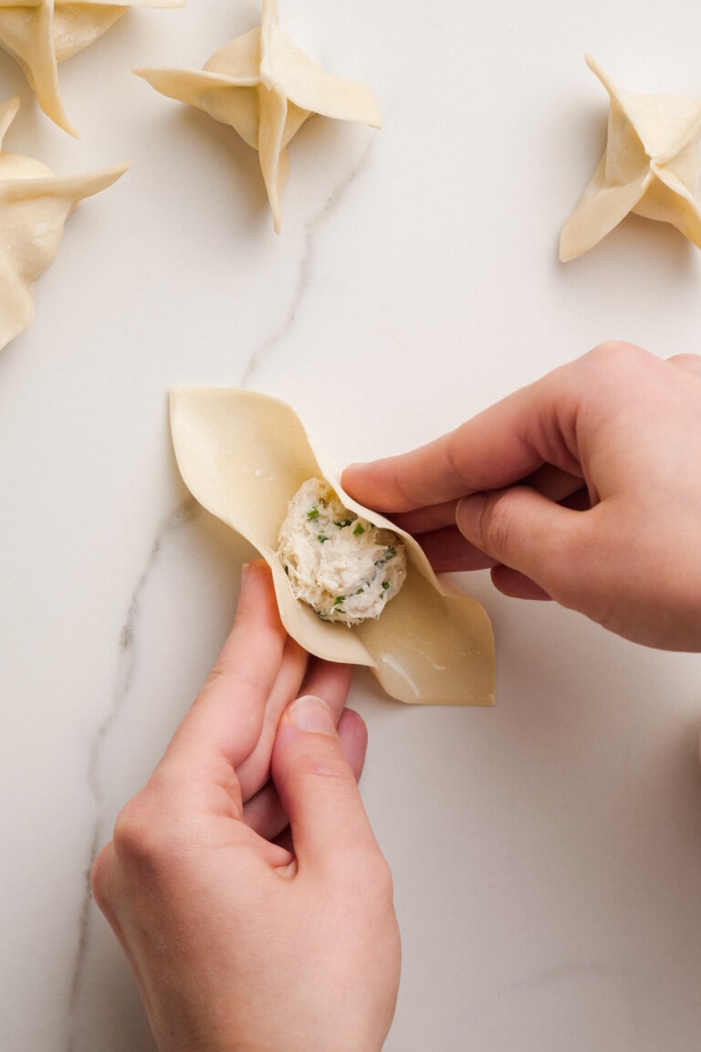wonton wrapper with spoonful of crab filling in the center. woman's hand starting to fold into a star