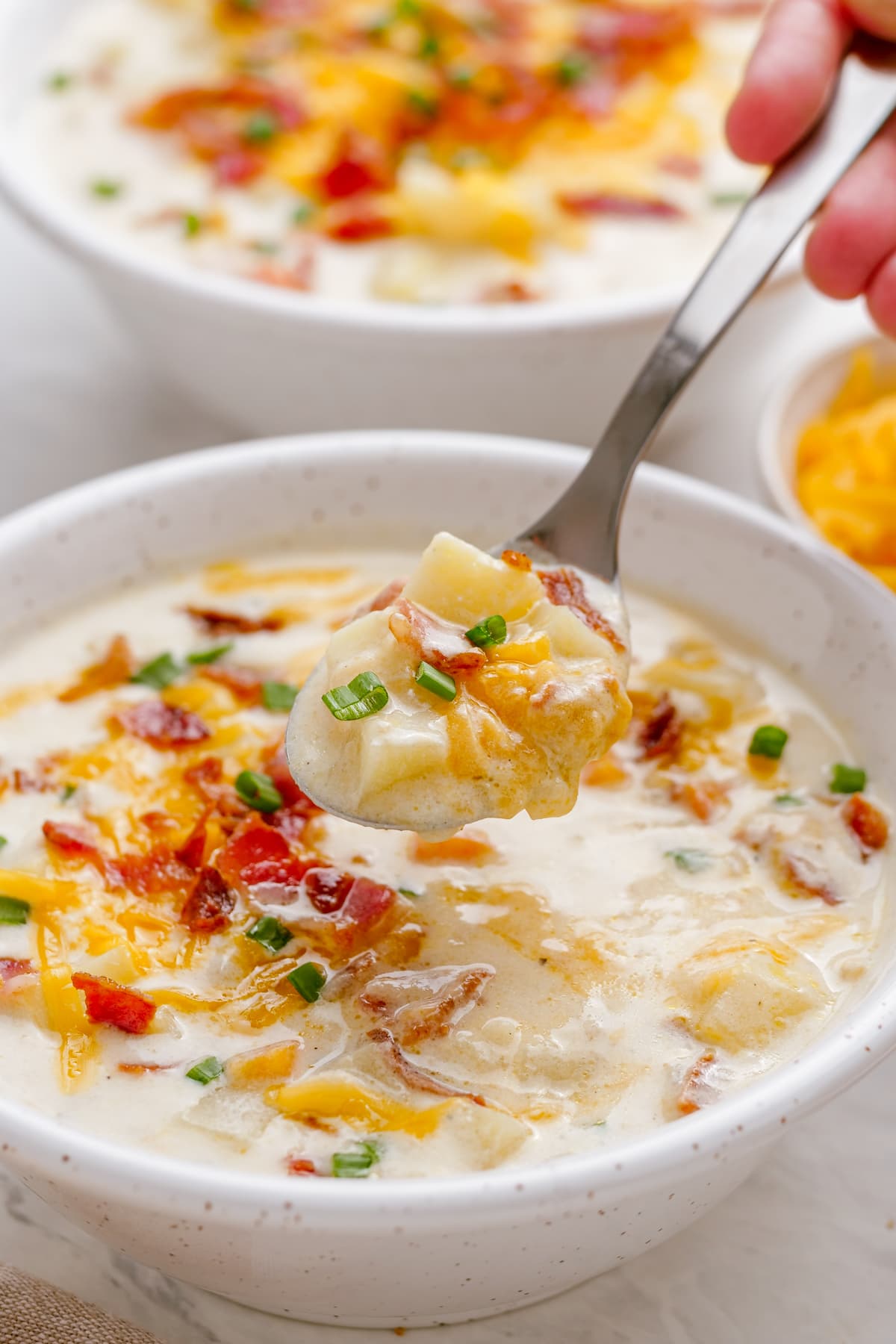 woman's hand spooning out loaded baked potato soup from single bowl