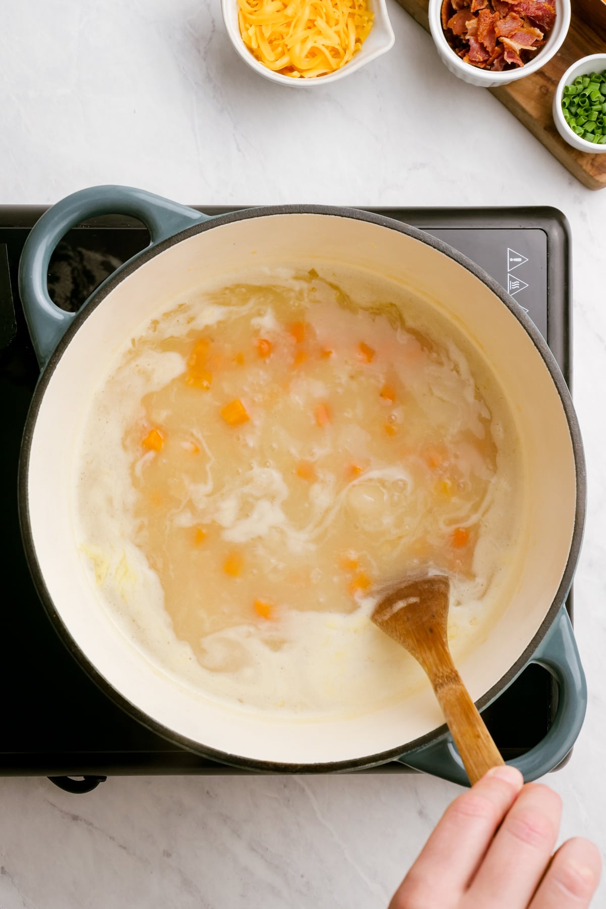 woman's hand stirring broth and vegetables in pot with wooden spoon