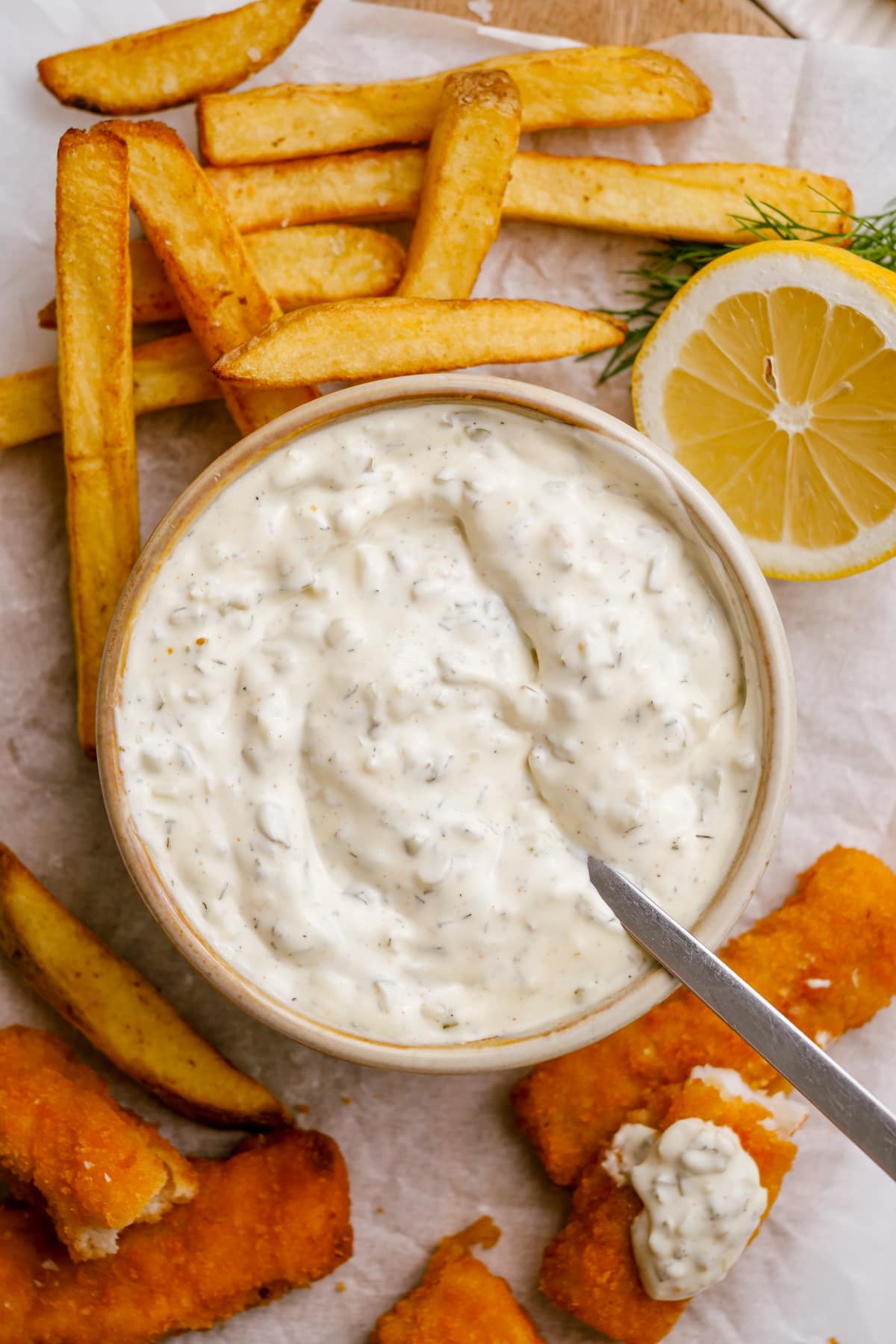 bowl of tartar-sauce with spoon with fish and fries surrounding