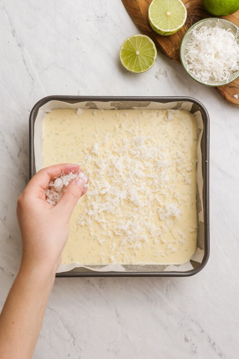 woman's hand sprinkling coconut over cream cheese mixture in baking dish