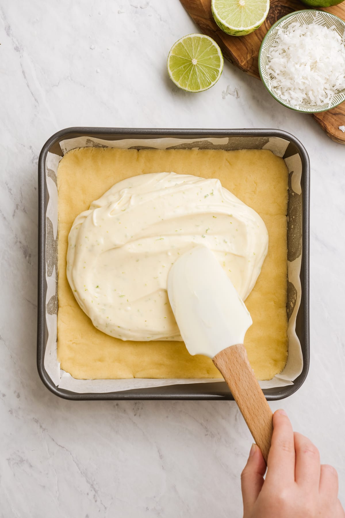 woman's hand spreading cream cheese mixture on top of sugar cookie dough in baking dish