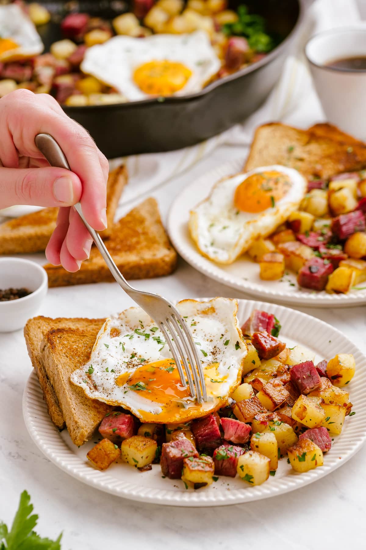 corned beef hash on a plate with a woman's hand cutting into the egg yolk