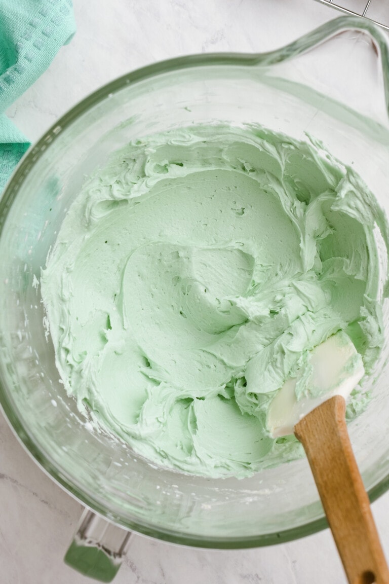light green frosting in a glass bowl with rubber spatula