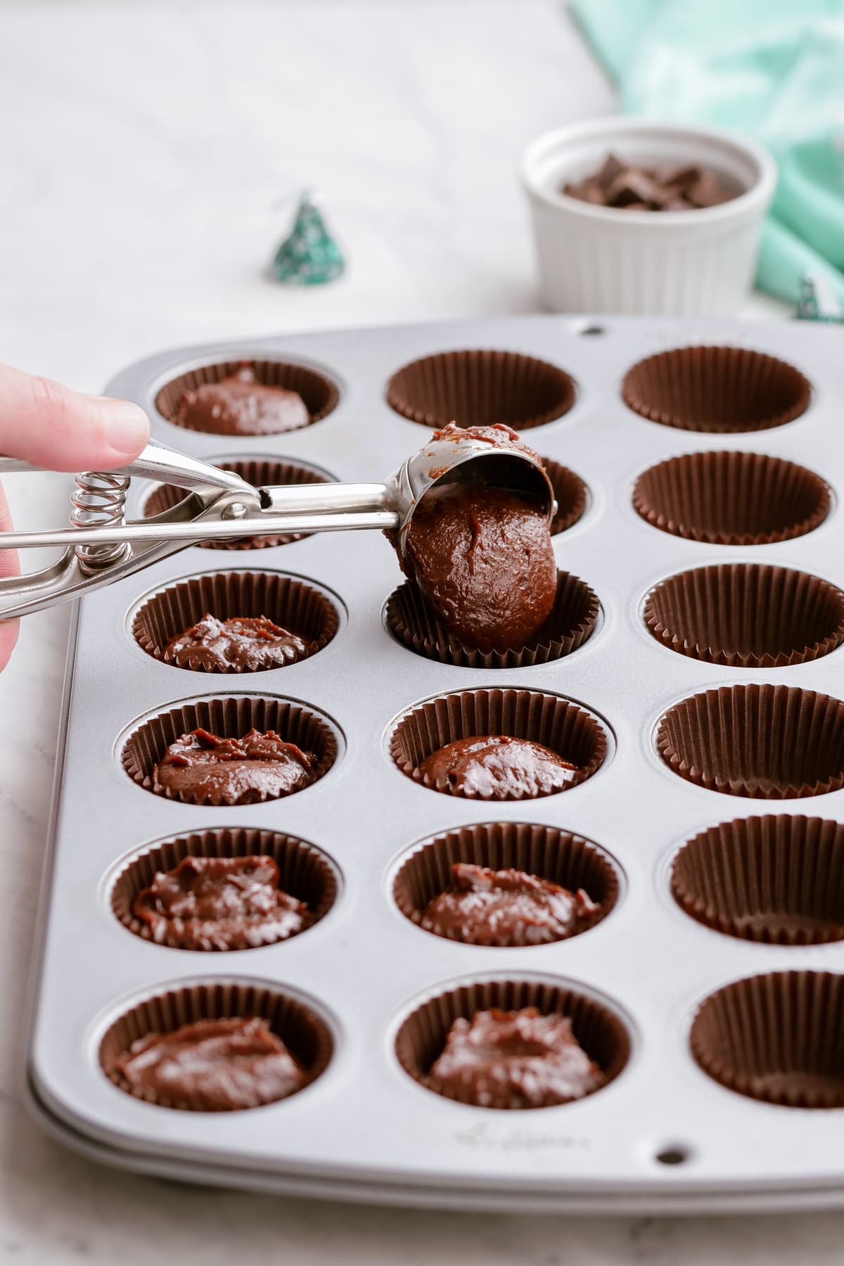 scooping brownie batter into mini muffin tins