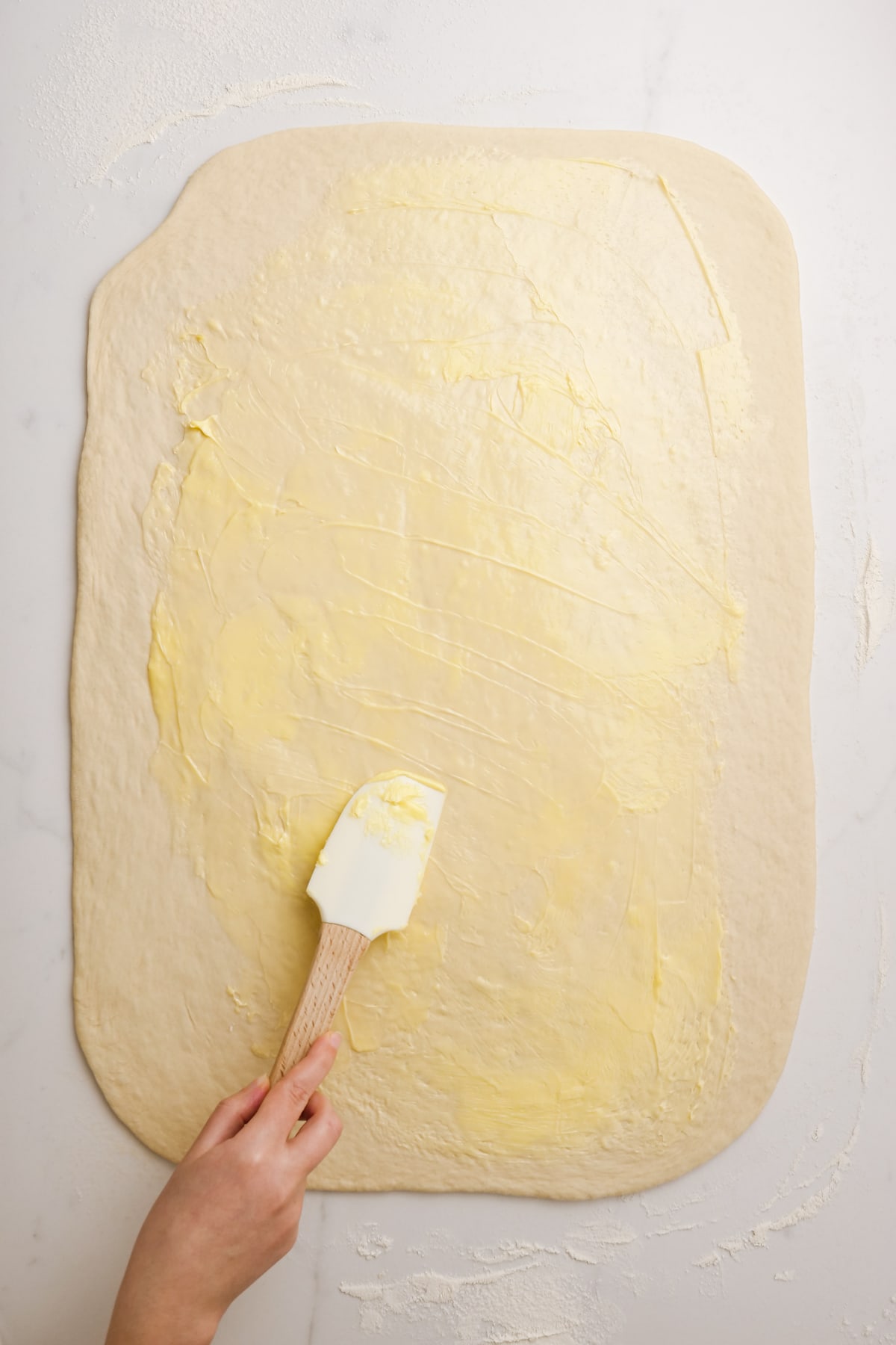 spreading butter on dough with rubber spatula