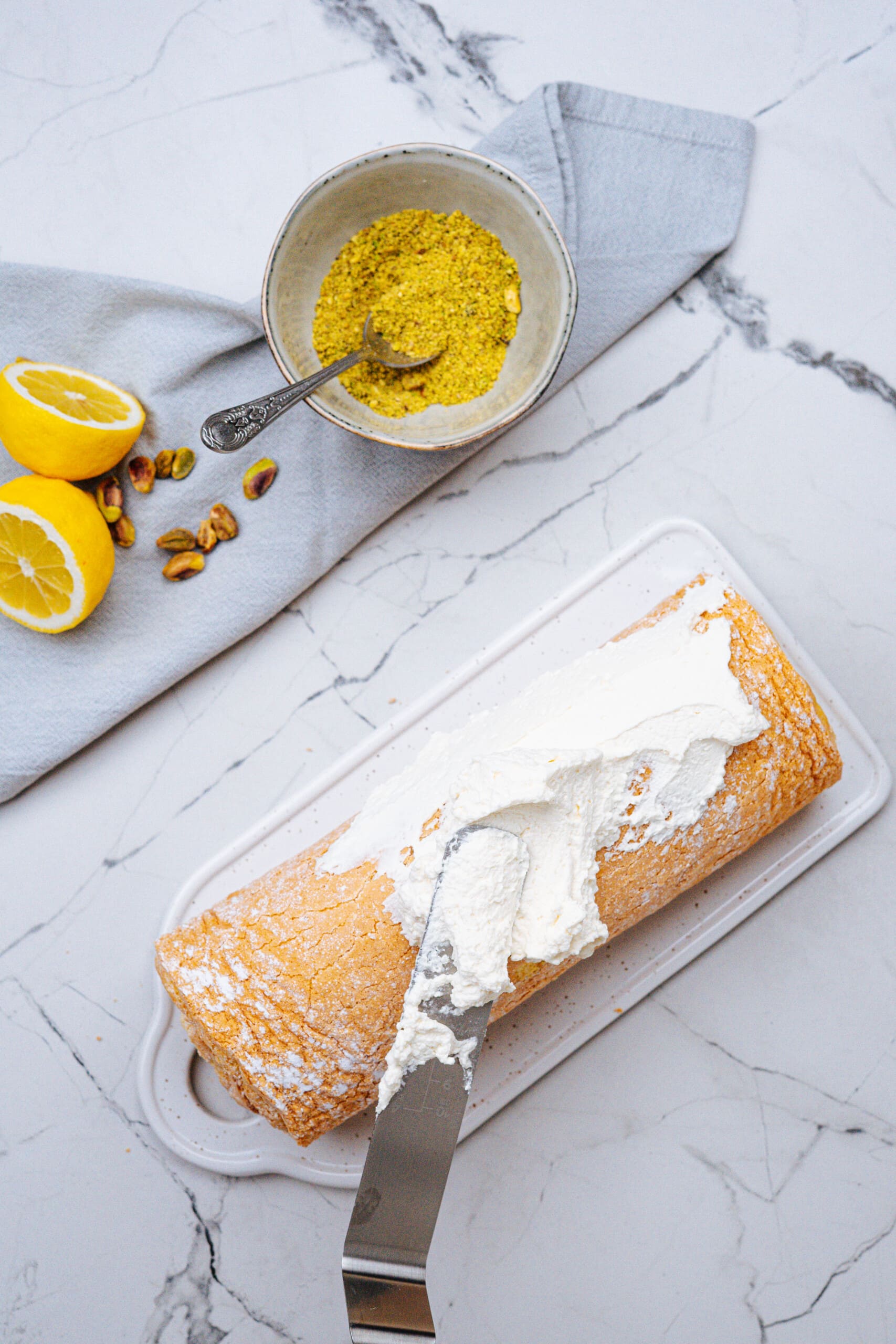 whipped topping being spread over the outside of pistachio lemon roll cake