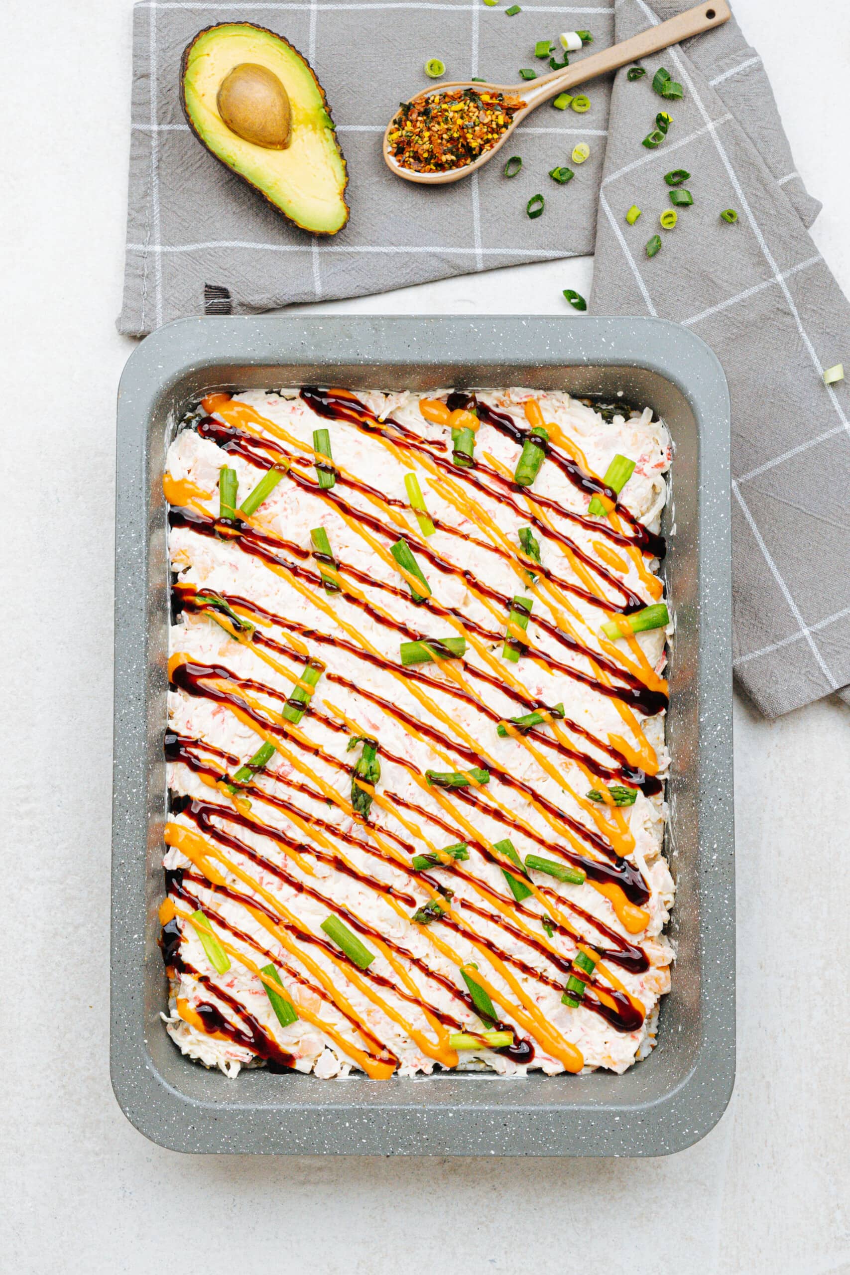 Sirracha sauce drizzled diagonally over the sushi casserole
