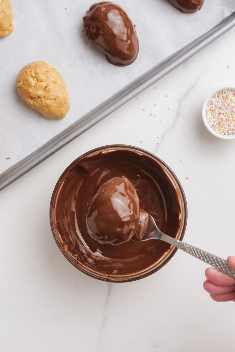 woman's hand dipping peanut-butter-easter-eggs-into melted chocolate