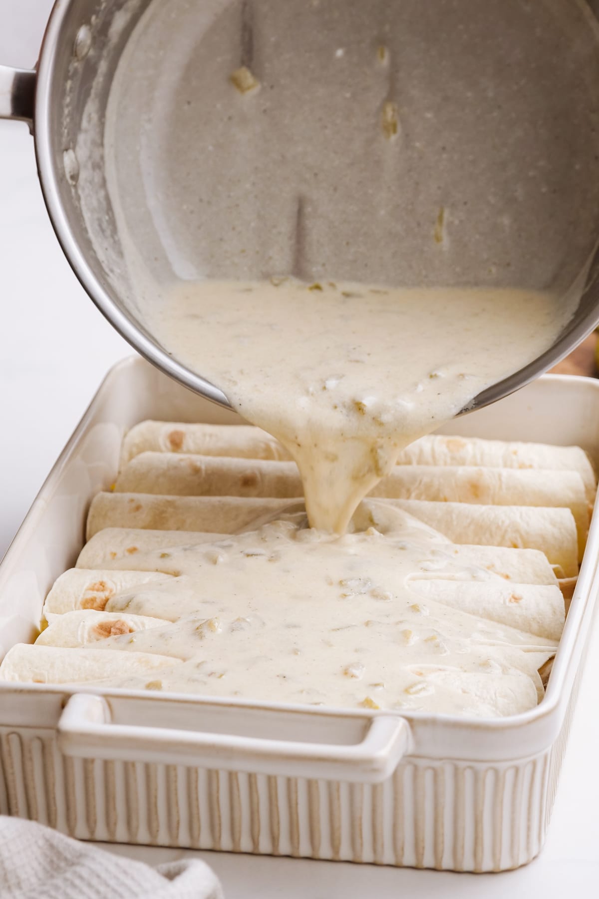 pouring sauce over rolled enchiladas in baking pan