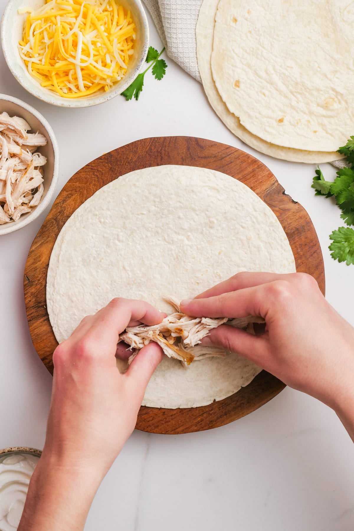 woman's hands adding shredded chicken to a tortilla