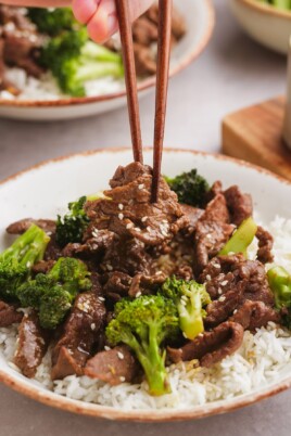 beef and broccoli on a plate with chop sticks grabbing a piece of beef