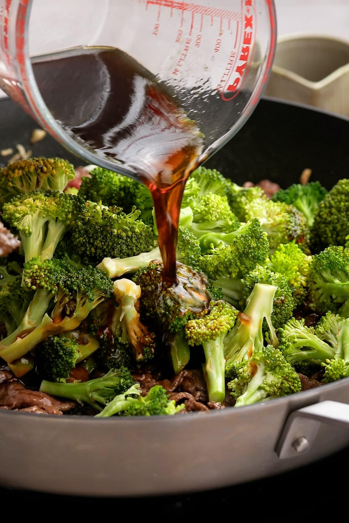 beef and broccoli in a skillet with sauce being poured over