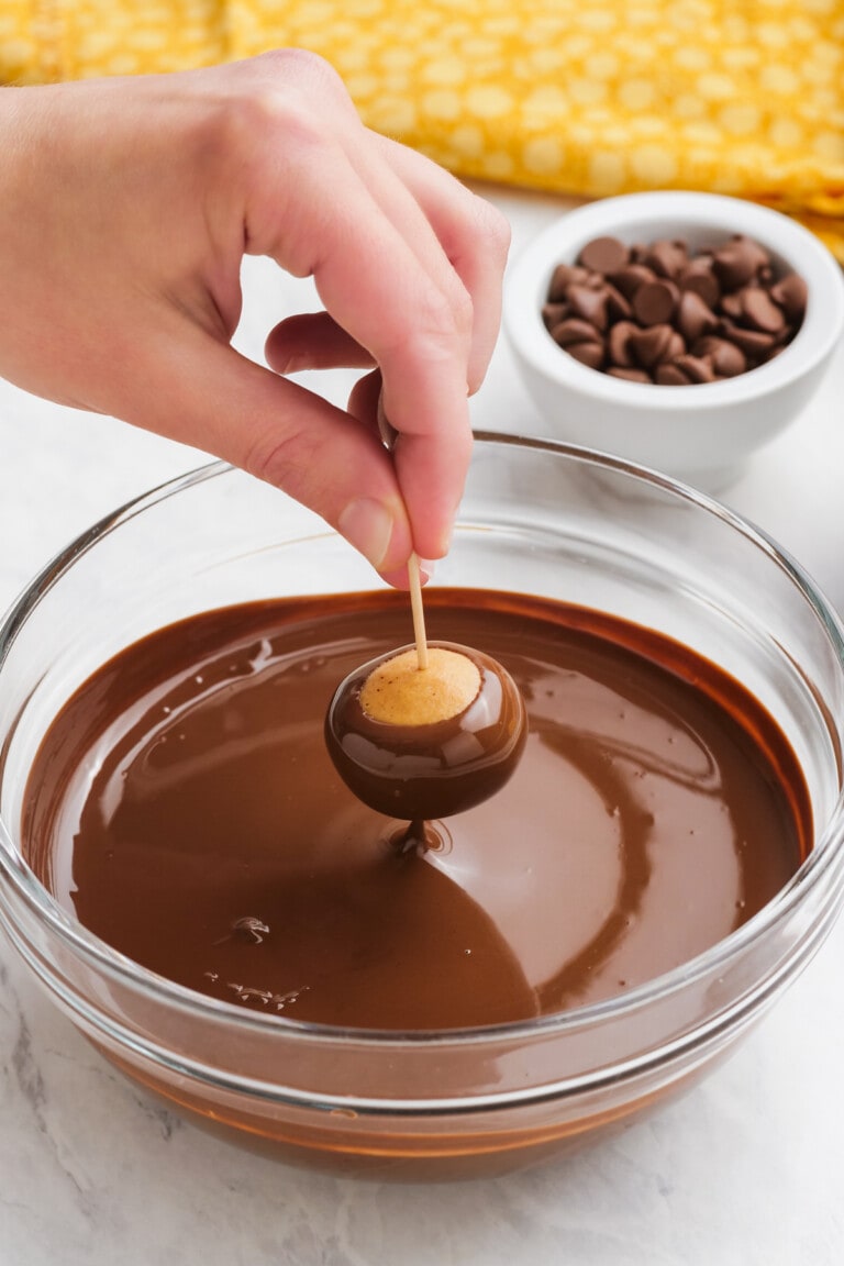 woman's hand dipping buckeye in chocolate