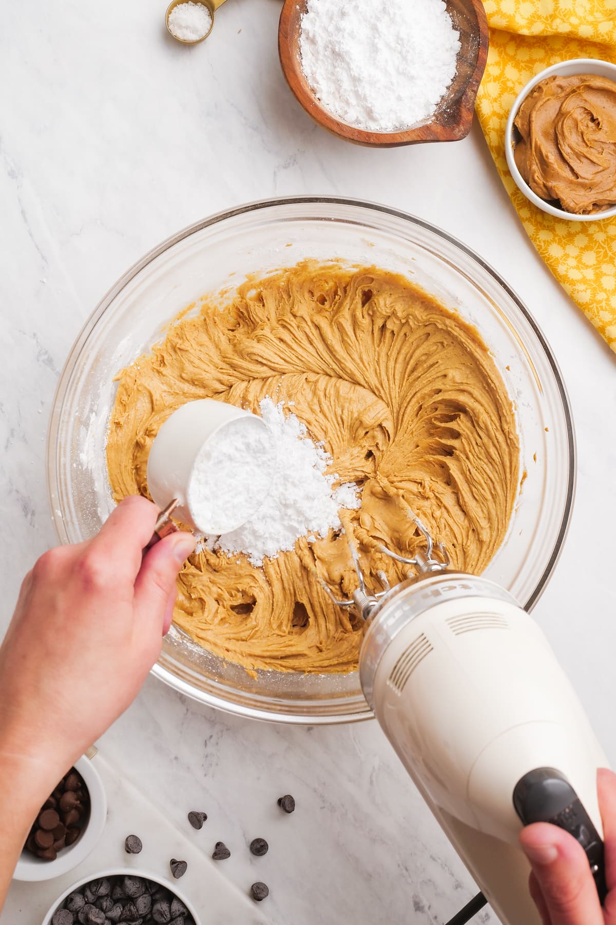 Woman's hand adding powdered sugar to peanut butter mixture while hand mixer is mixing