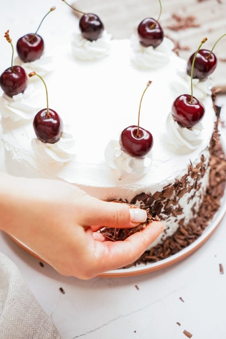 woman's hand placing the chocolate shavings along the sides of the cake