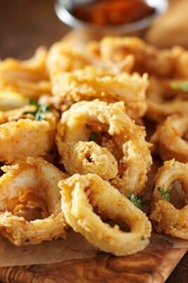 Fried calamari with a piece of lemon and a small bowl of dip on a wooden serving tray