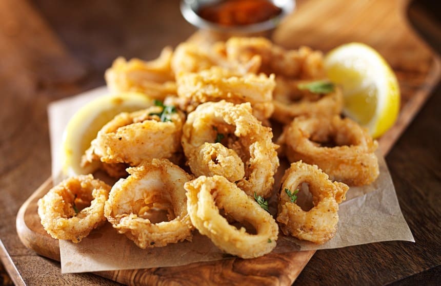 Fried calamari with a piece of lemon and a small bowl of dip on a wooden serving tray