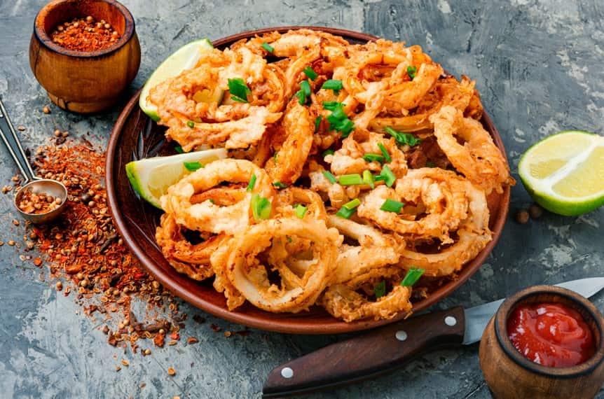 Calamari on a plate with spices, pieces of lime, and some dip, next to a knife