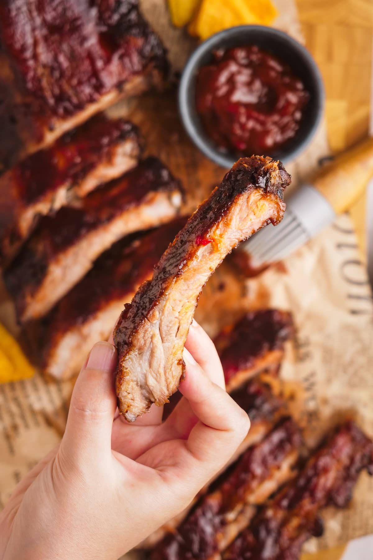 woman's hand holding one rib over top of oven baked ribs sliced on serving board