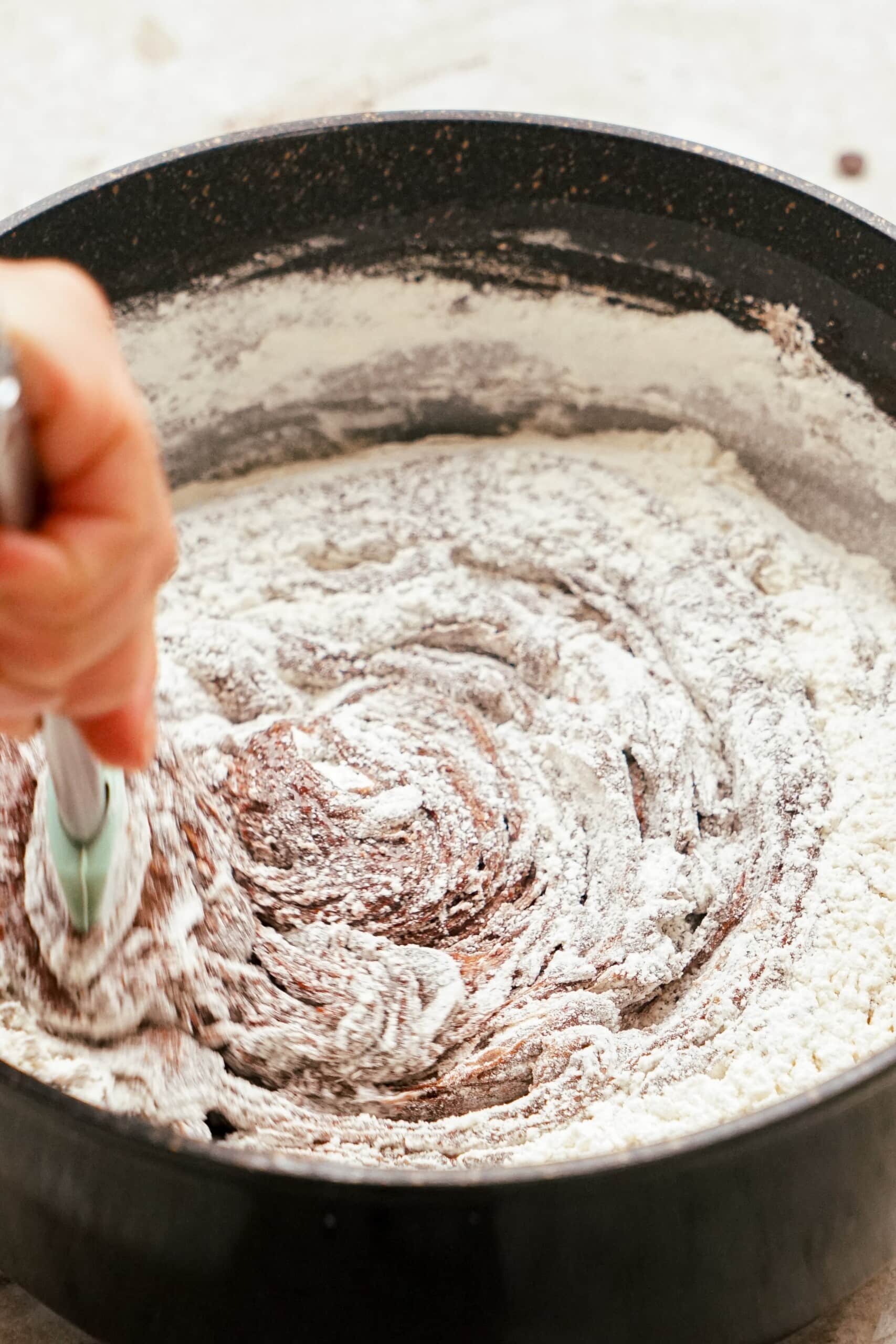 woman's hand stirring in dry ingredients to brownie mixture