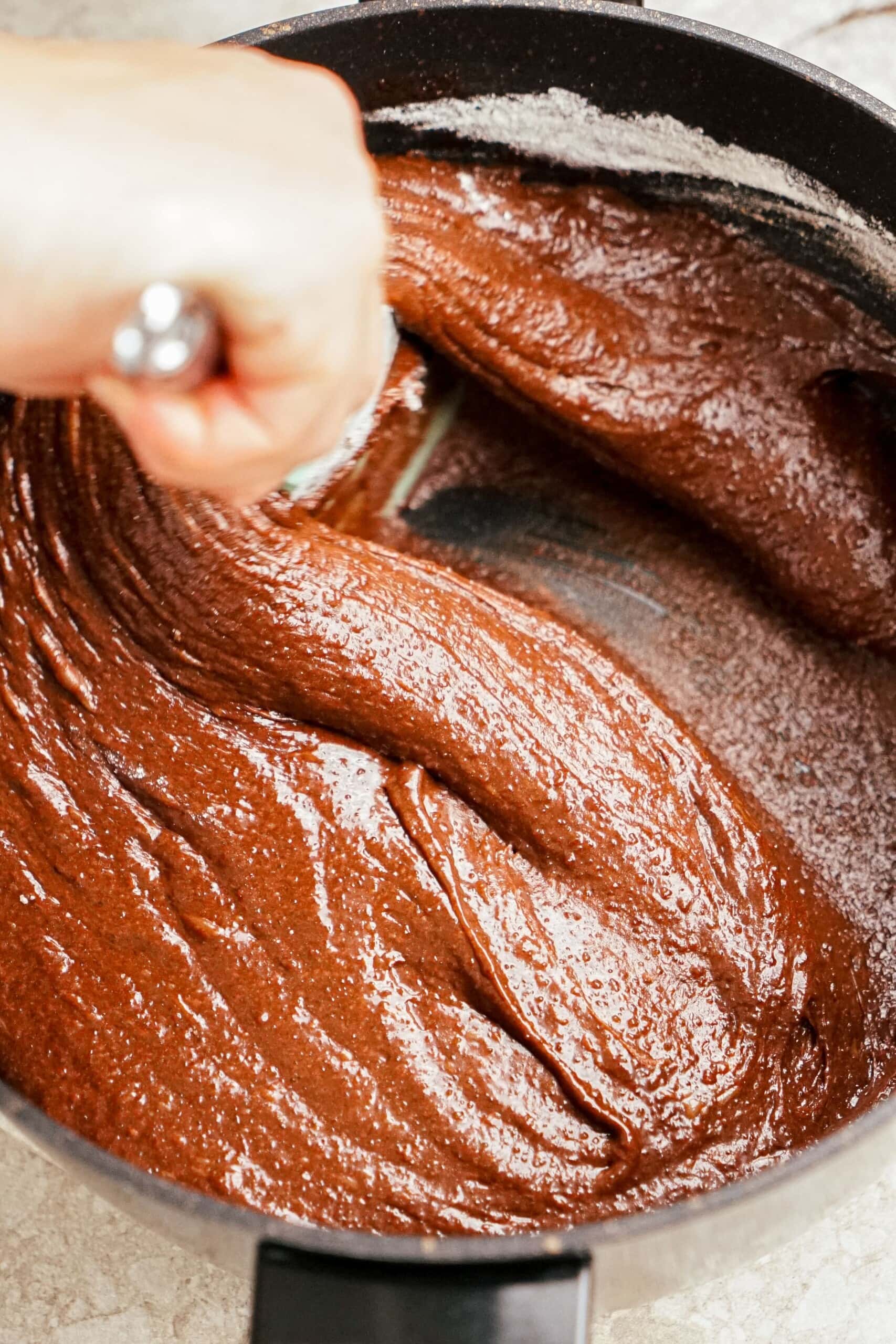 woman's hand mixing dry ingredients into brownie mixture