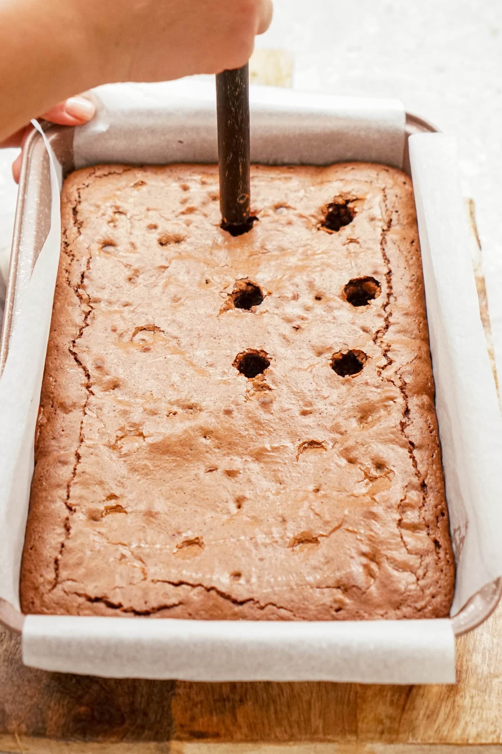 poking holes into brownies with the end of a wooden spoon