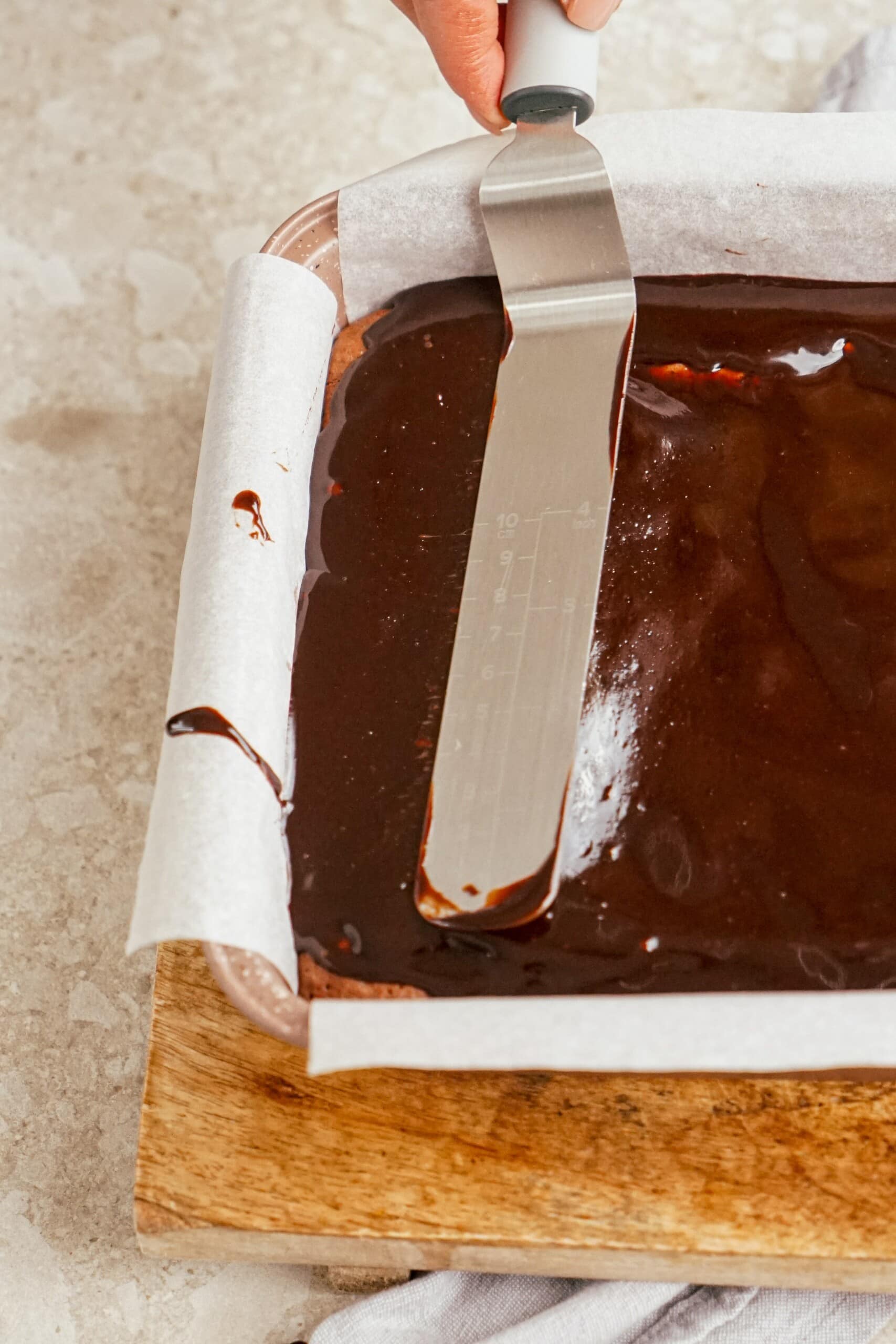 smoothing out hot fudge over brownies with an offset spatula