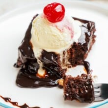 hot fudge brownie on a plate with vanilla ice cream and a cherry on top