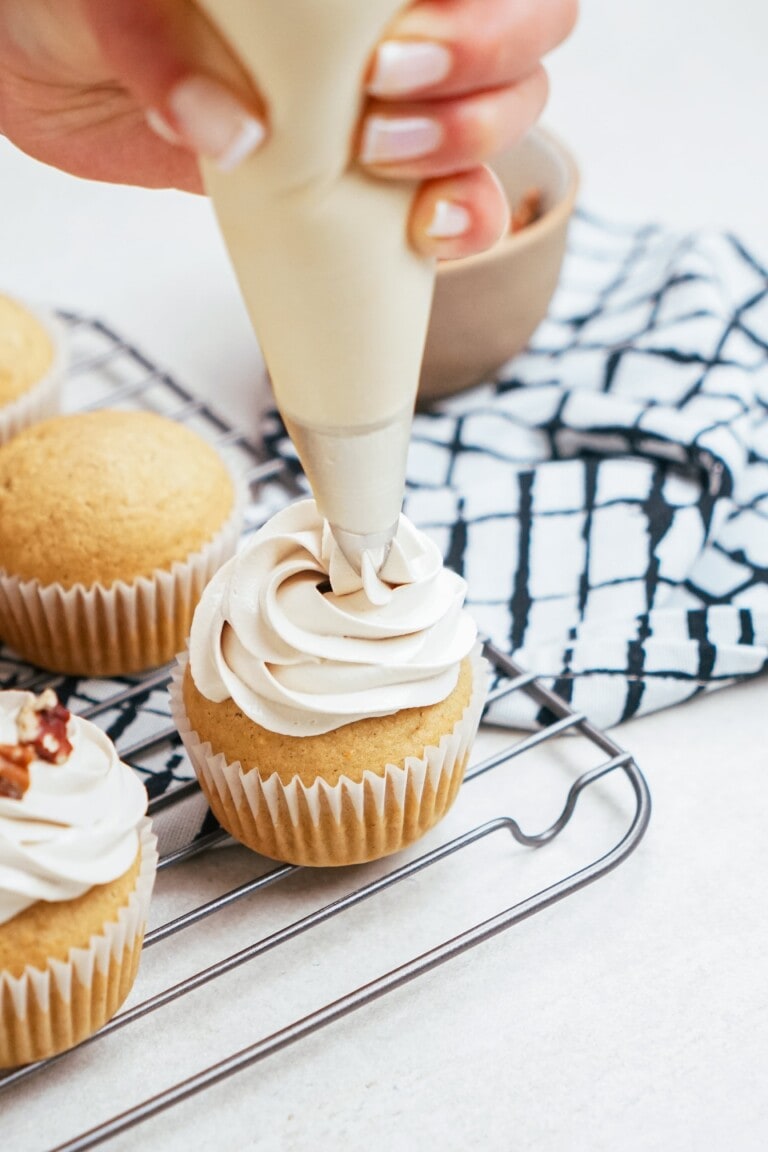 womans hand piping frosting onto a cupcake