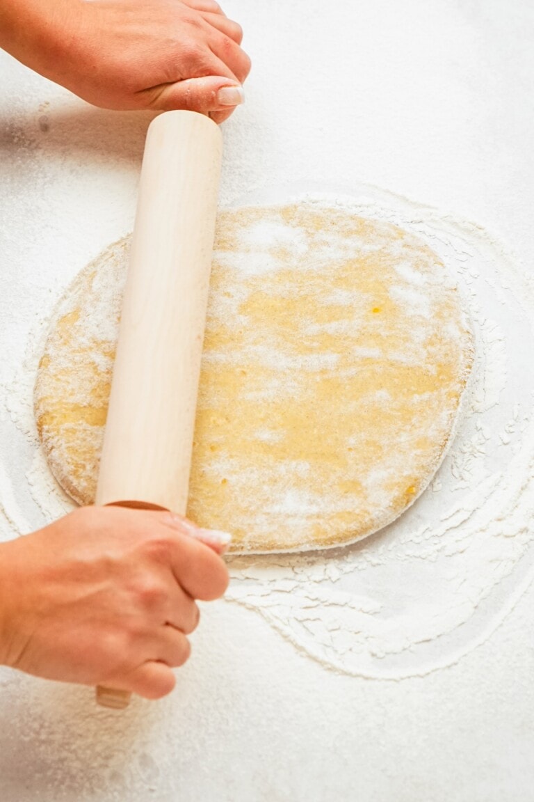 woman's hands using a rolling pin to roll out donut dough