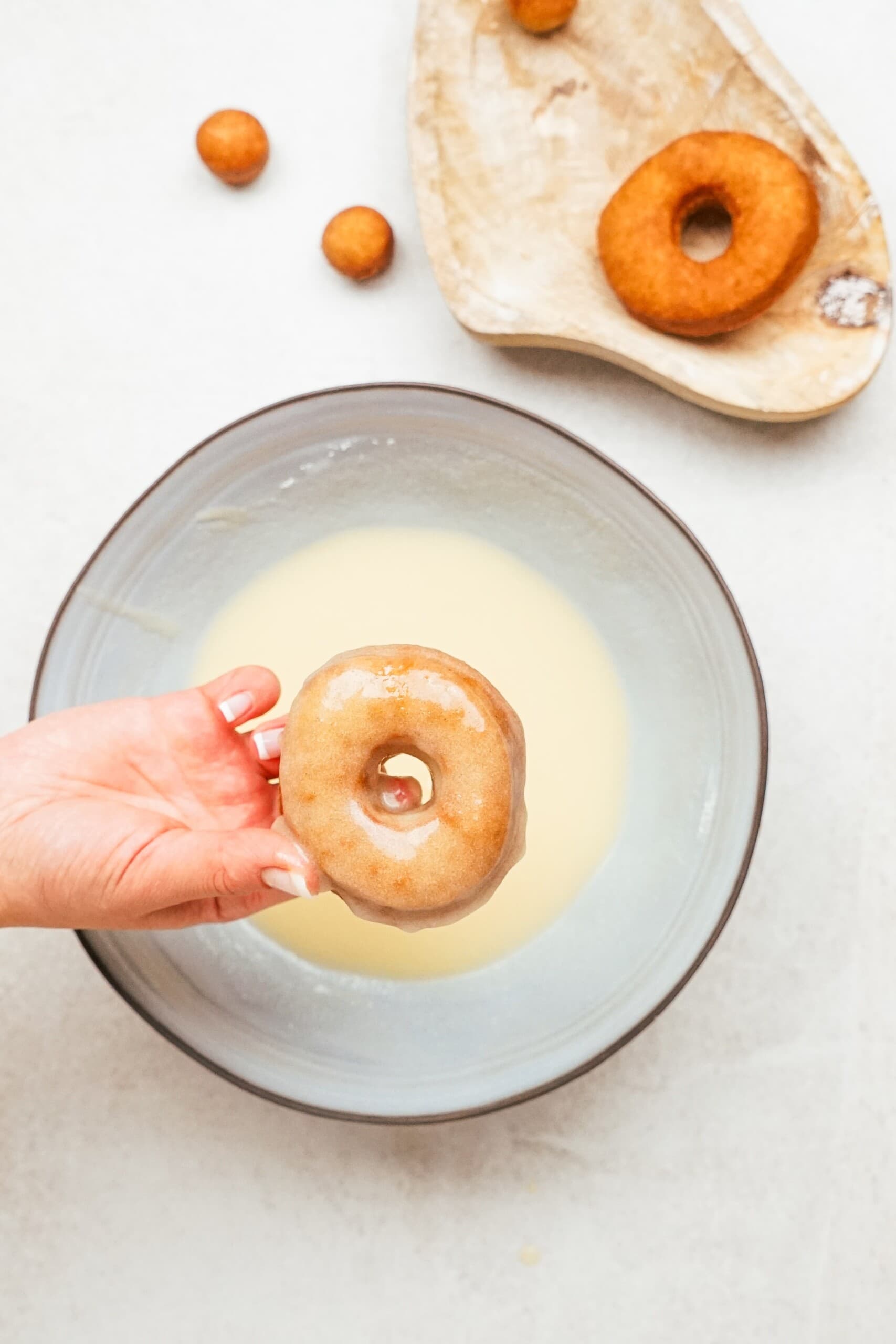 woman's hand dipping a donut into the glaze