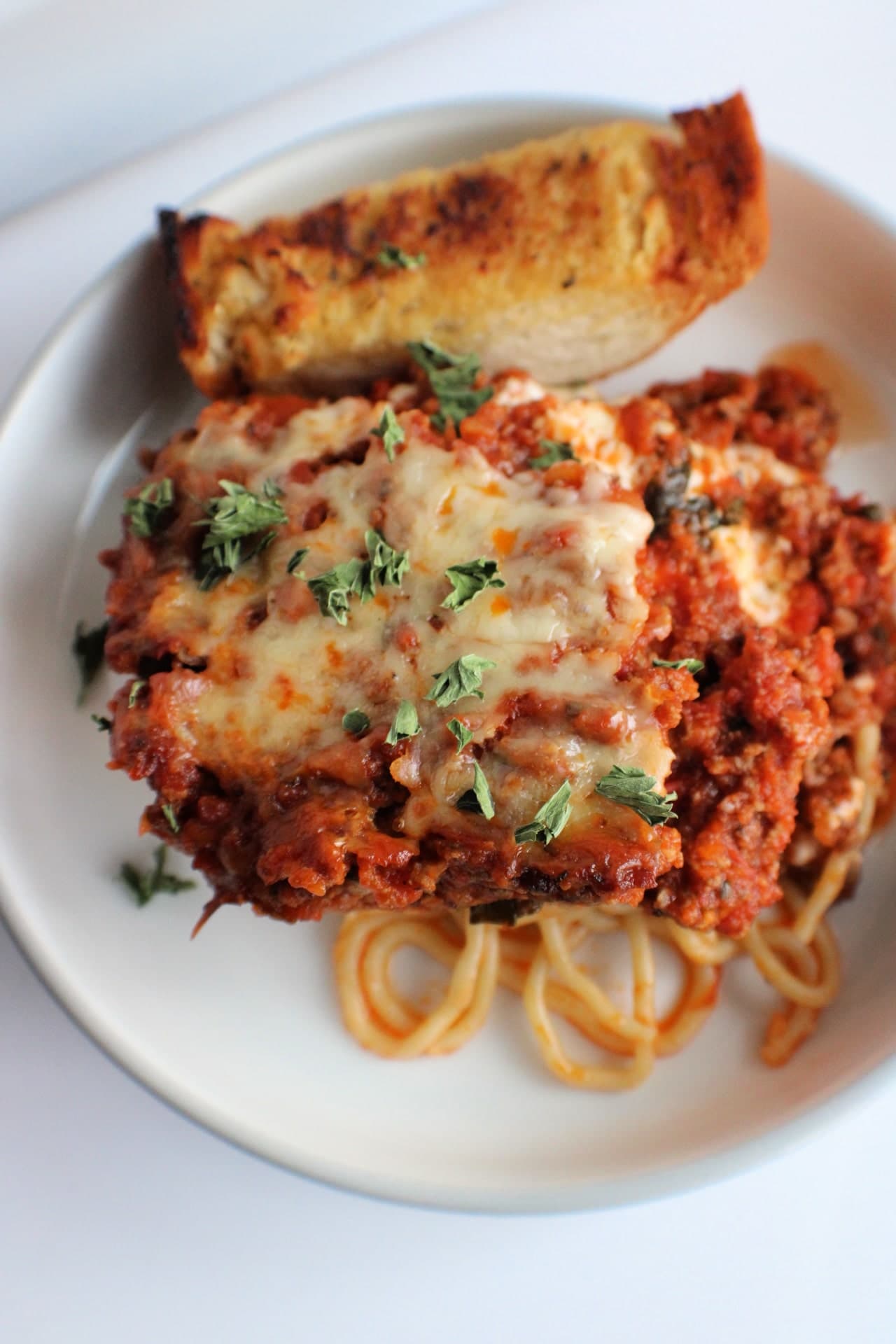 baked spaghetti casserole on a plate with garlic bread
