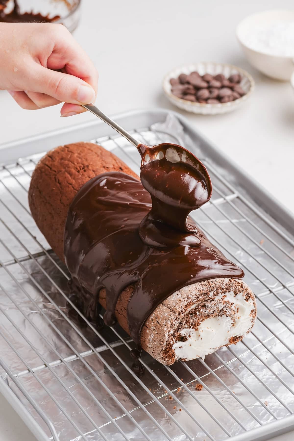 chocolate swiss roll with glaze being spooned over the top
