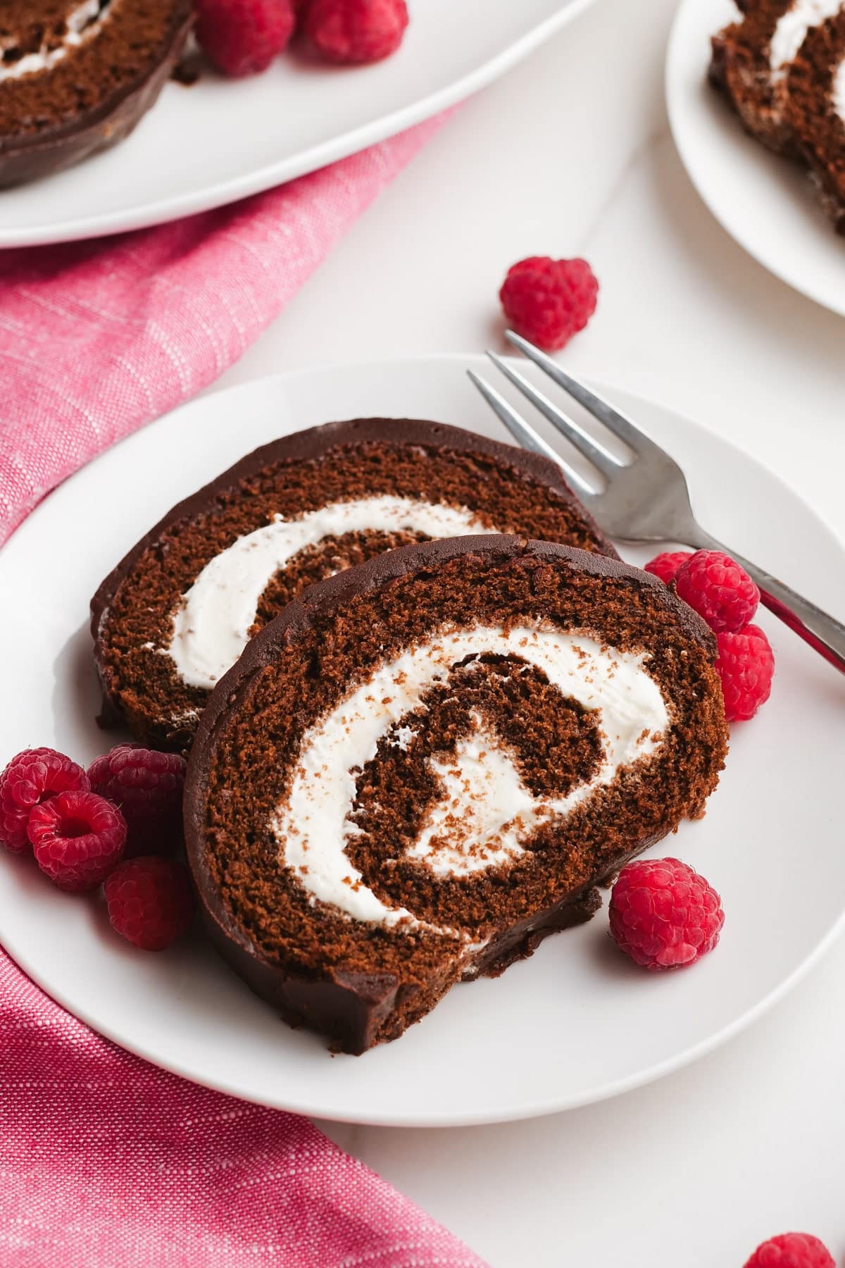 chocolate swiss roll slices on a plate with raspberries and a fork
