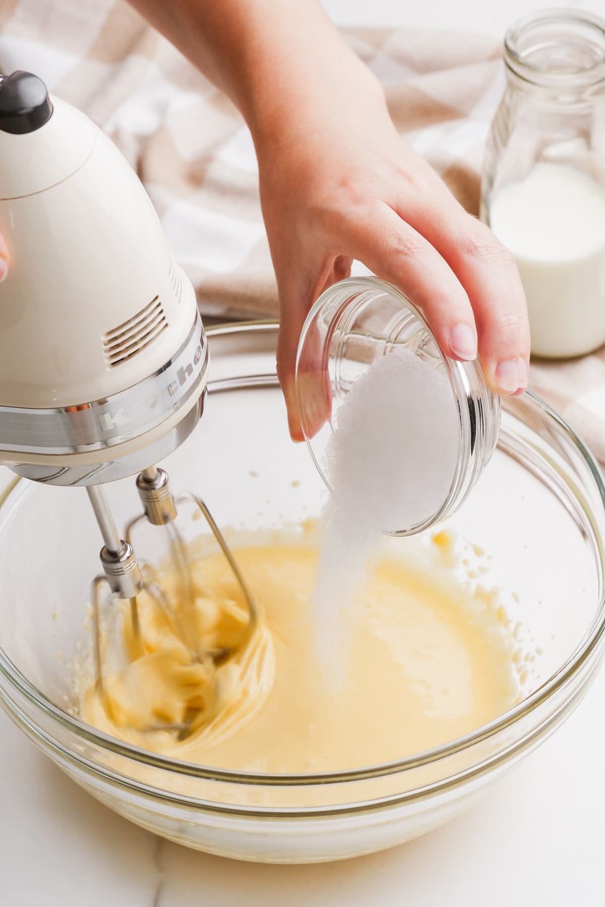 cake batter with woman's hand adding sugar while mixing