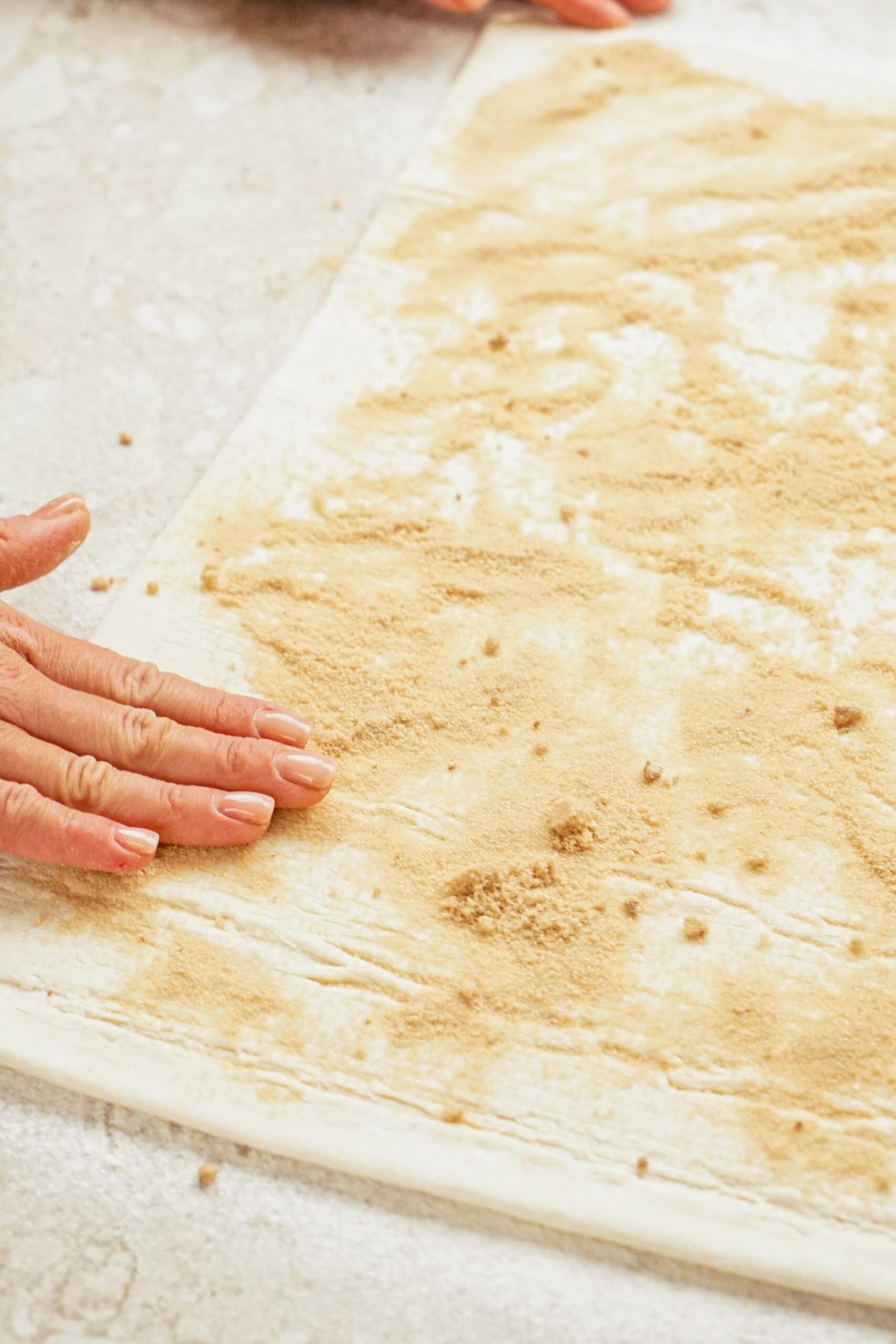 Woman's hand pressing brown sugar and cinnamon mixture onto Puff Pastry sheet