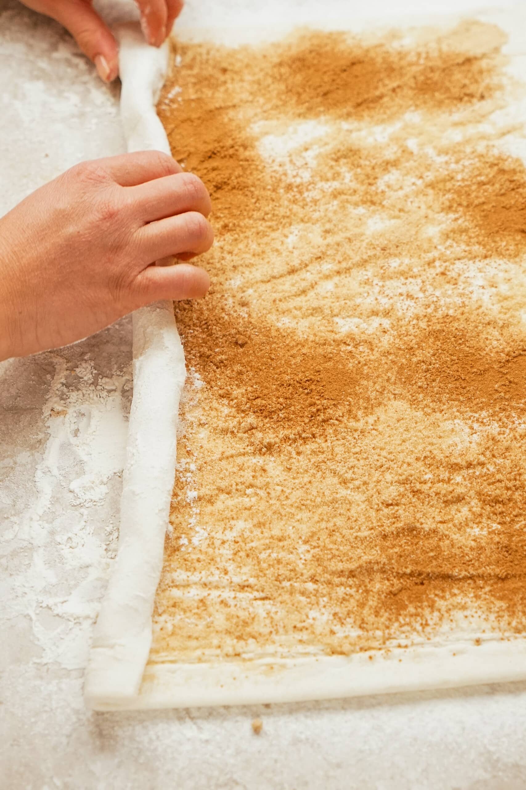 Woman's hand rolling Puff Pastry sheet with brown sugar and cinnamon mixture