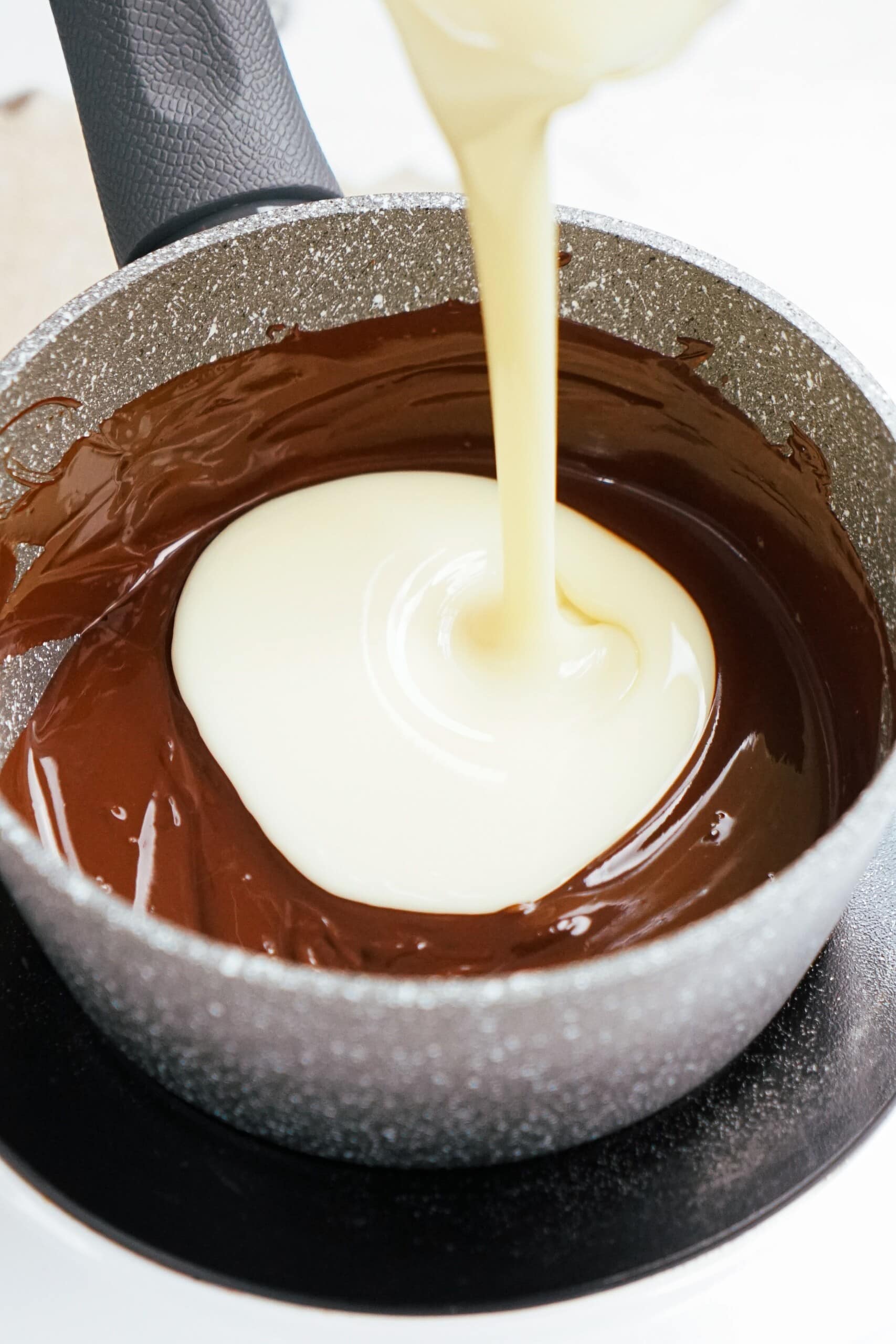 sweetened condensed milk pouring into melted chocolate in a pot.