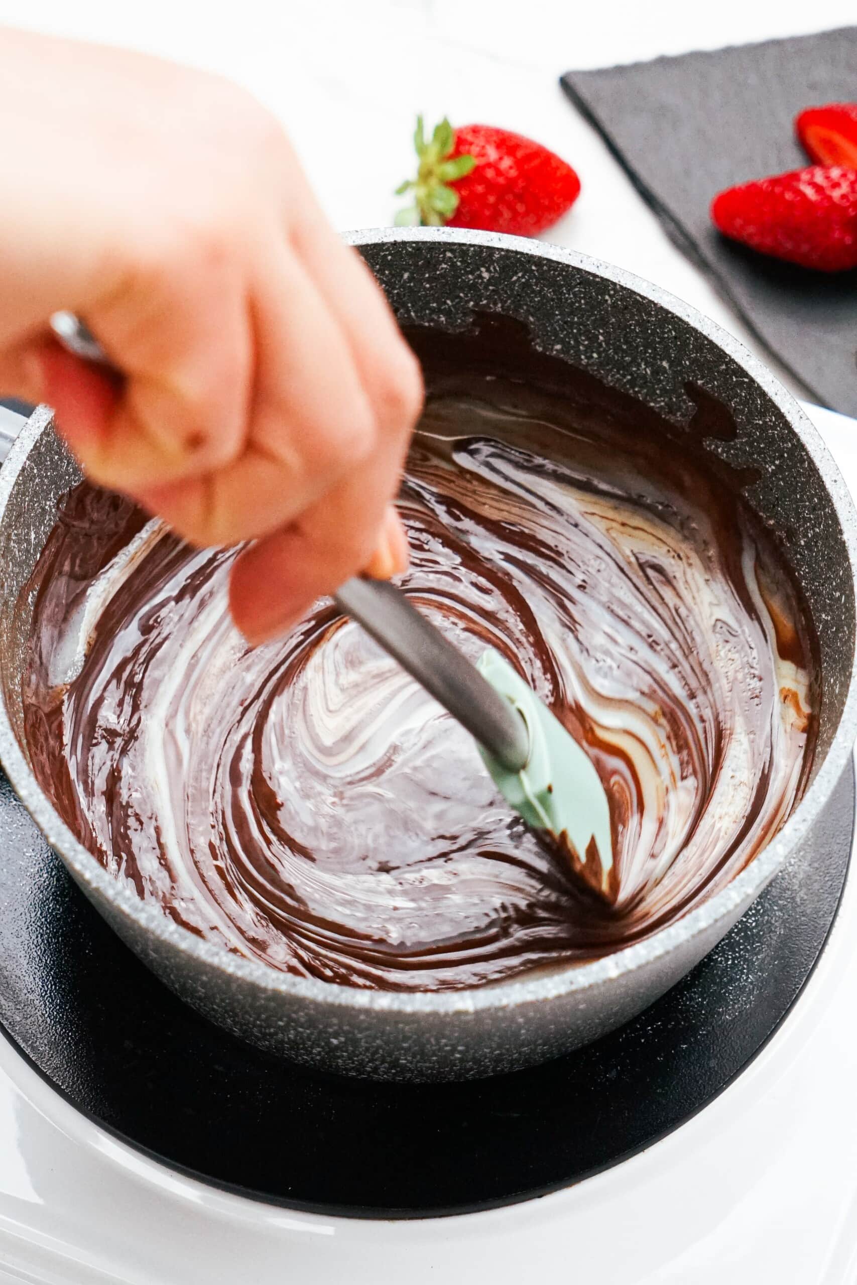 woman's hand stirring dipping chocolate ingredients in sauce pot.