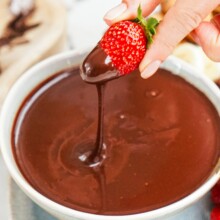 woman's hand dipping a strawberry into a bowl of chocolate.